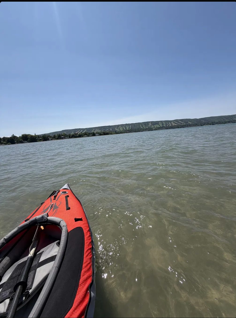 A kayak on the calm open water of Georgian Bay, with the Blue Mountain escarpment and ski runs across the bay